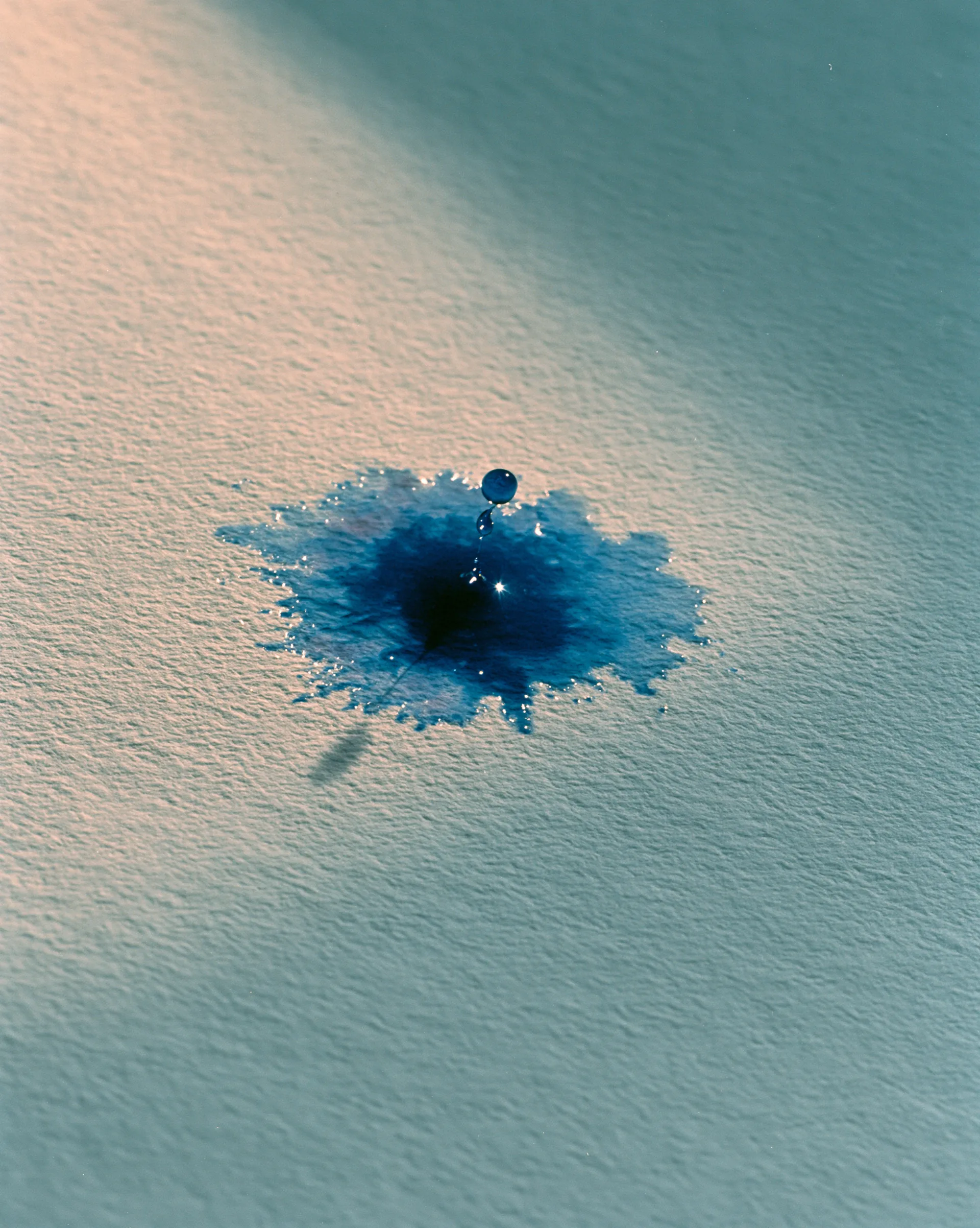 Macro of a single deep-blue ink drop blooming on cream paper.